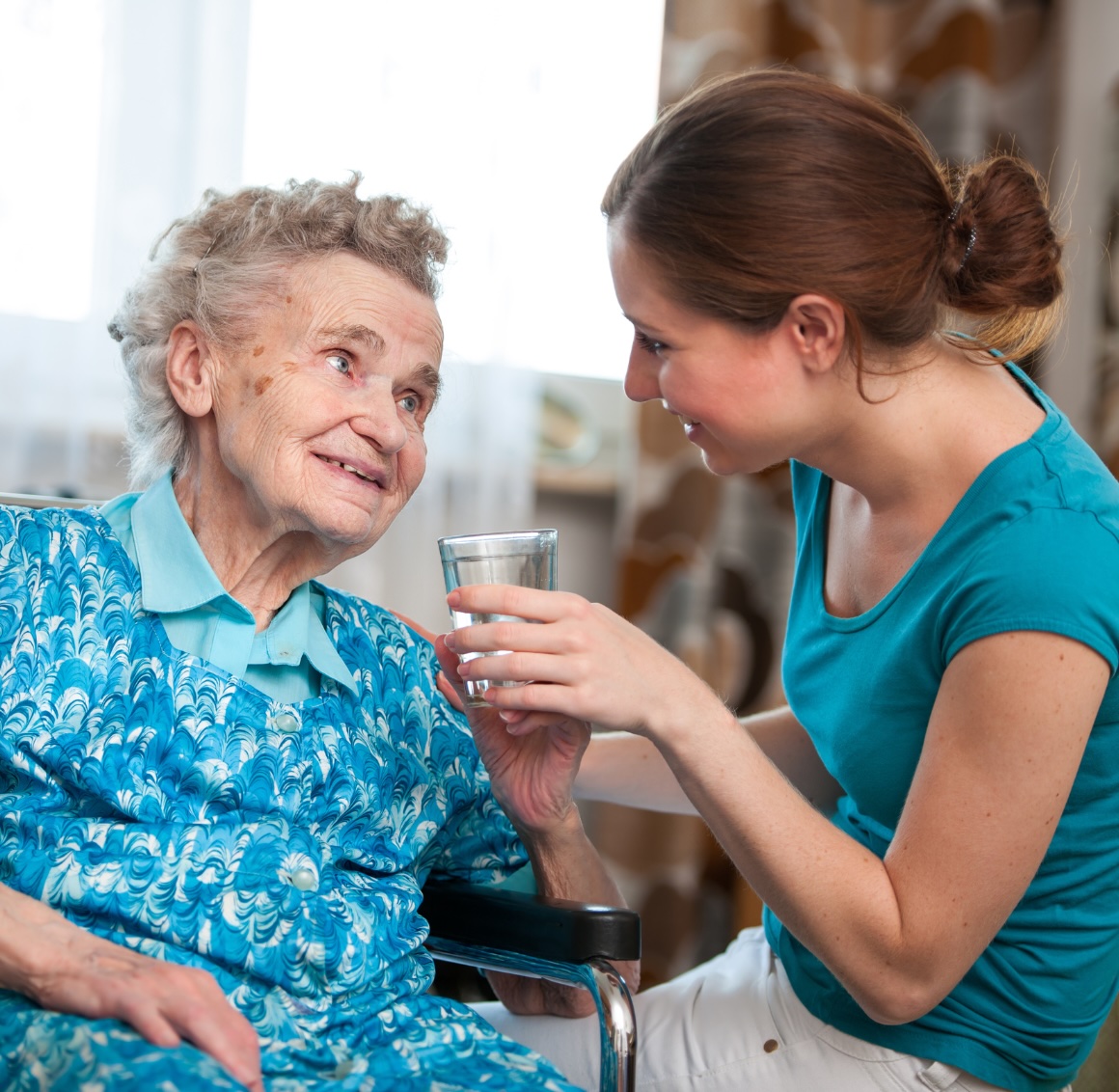 A caregiver cares for an older client by providing a glass of water representing the respite care services provided in Orange, VA.