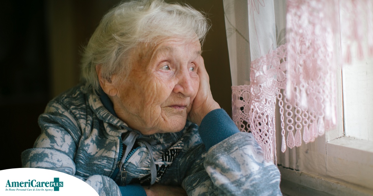 An older woman peacefully looks out of the window while the sun is still up, representing what can happen with sundowning.